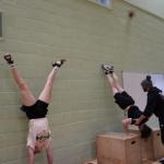 Students doing handstands against wall with trainer