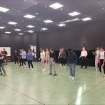 Numerous students in dance studio following instructor