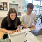 2 students participating in The Richard Huish College Dragons Den 2024. Both are working on laptops.