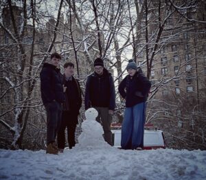 Four students stood around a snowman they have built in Central Park, New York. Frosty trees are behind them