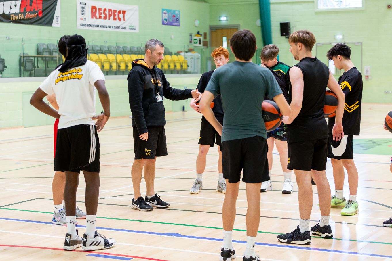 A basketball coach chatting with his team in the Huish sports hall.