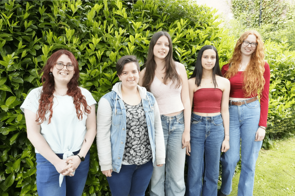 Five students stood in a row in front of a hedge. All have received offers for competitive university courses.