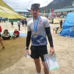 Albie at the end of the race, holding a certificate and wearing a medal. A couple of tents are in the frame.