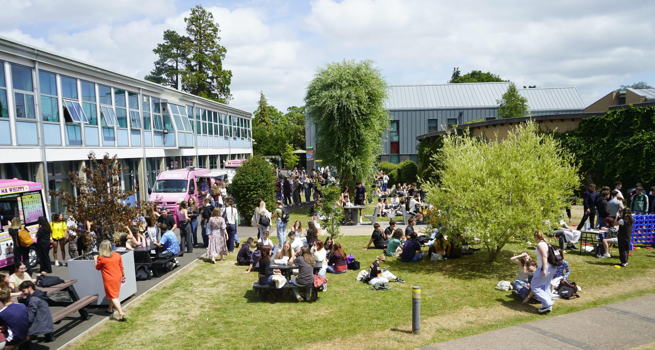 A wide shot of willow green in the sun with students at around eating, some are queueing for ice cream or doughnuts