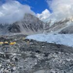 A snowy and misty scene of Everest. Small tents can be seen on the left hand side.