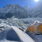 Tents covered in ice in the foreground, with mountain peaks in the background.