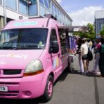 Students queue up next to a bright pink doughnut van