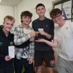Four students gathered around a small gold trophy.