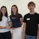 2 students gathered around a silver trophy