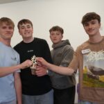 4 students gathered around a small trophy.