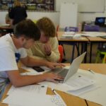 2 students sat working around a laptop