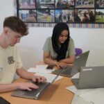 2 students sat working at a laptop