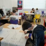 A student sat writing on a large piece of paper