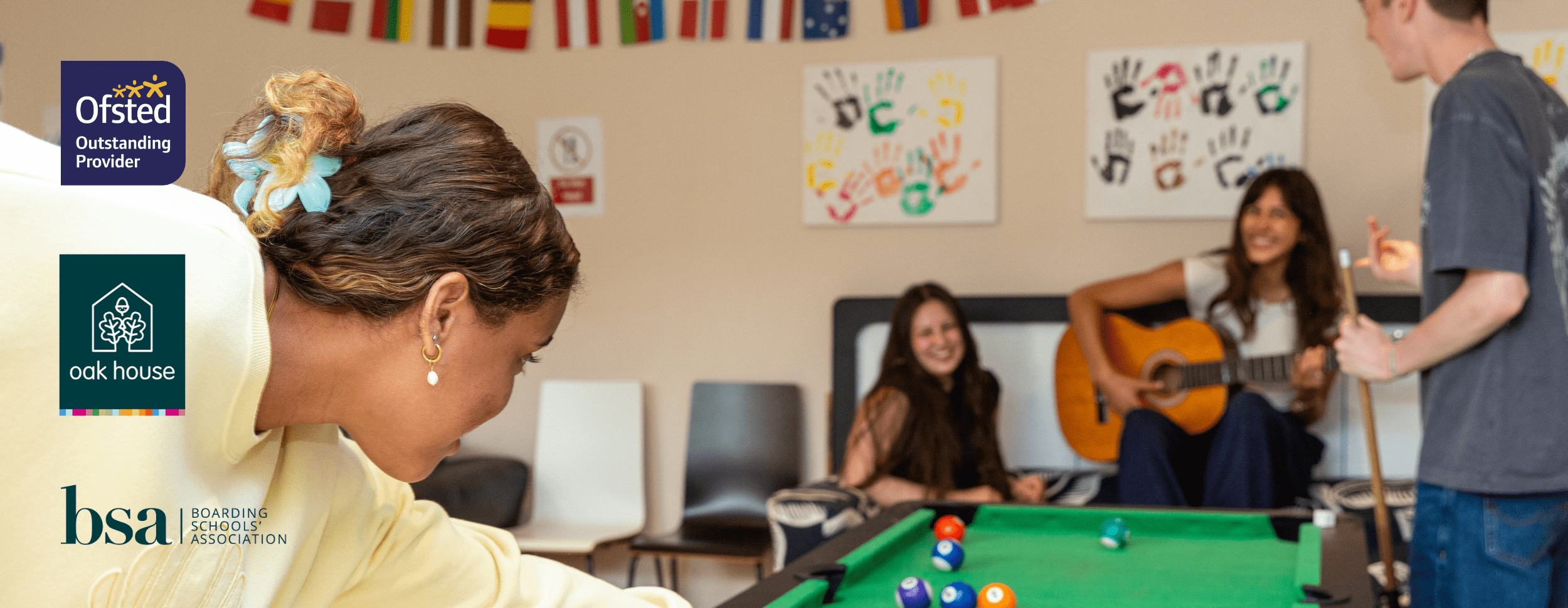 4 students smiling, one playing pool, another playing the guitar