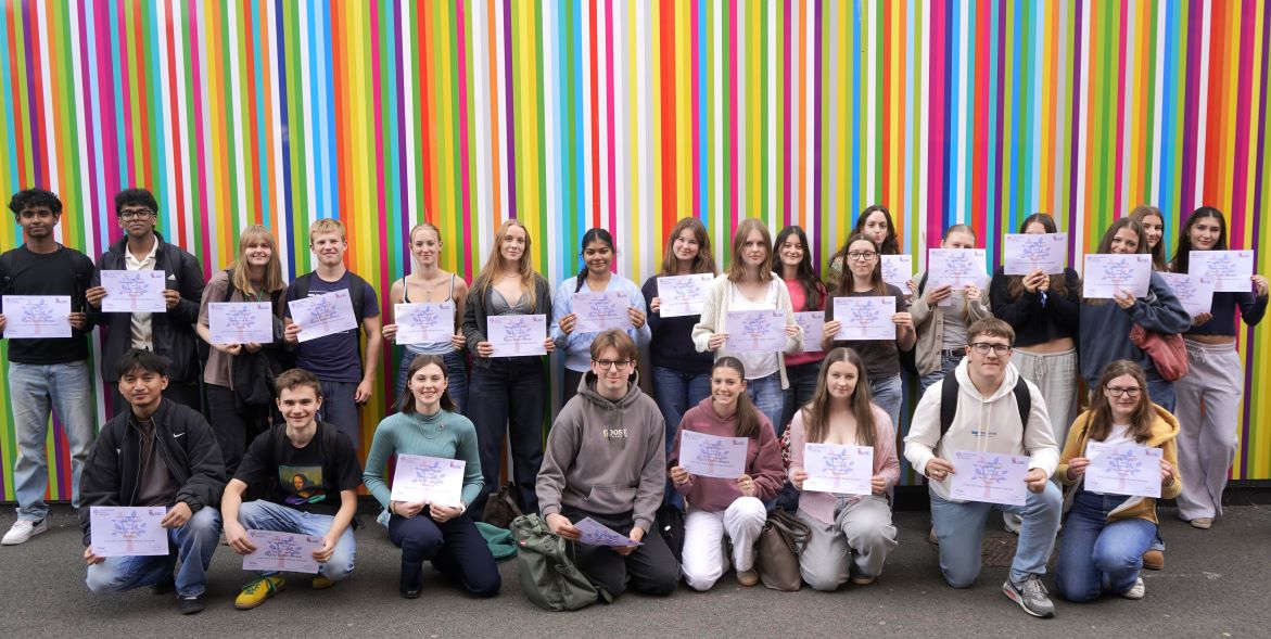 Group of students holding certificates and smiling, standing in front of a vibrant multicoloured striped background.