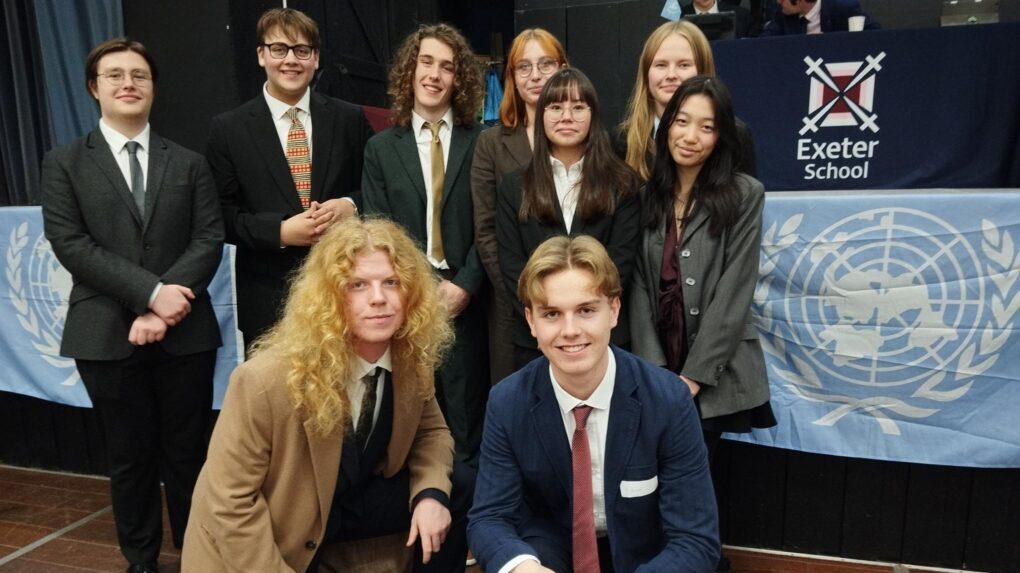 Nine students from Huish's MUN programme, dressed smartly and stood in front of a stage