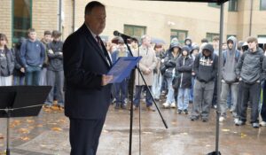 Kelvin Edwards gives a speech with a microphone, under a gazebo, with students and staff looking on.