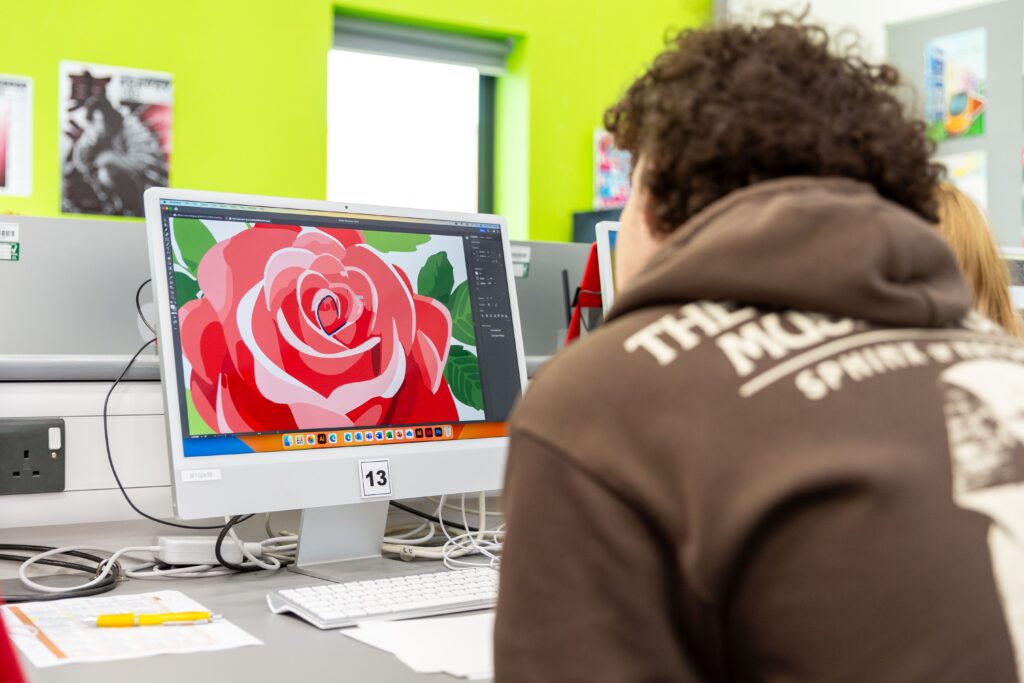 A student sits in front of an IMac, on the screen is a large rose graphic.