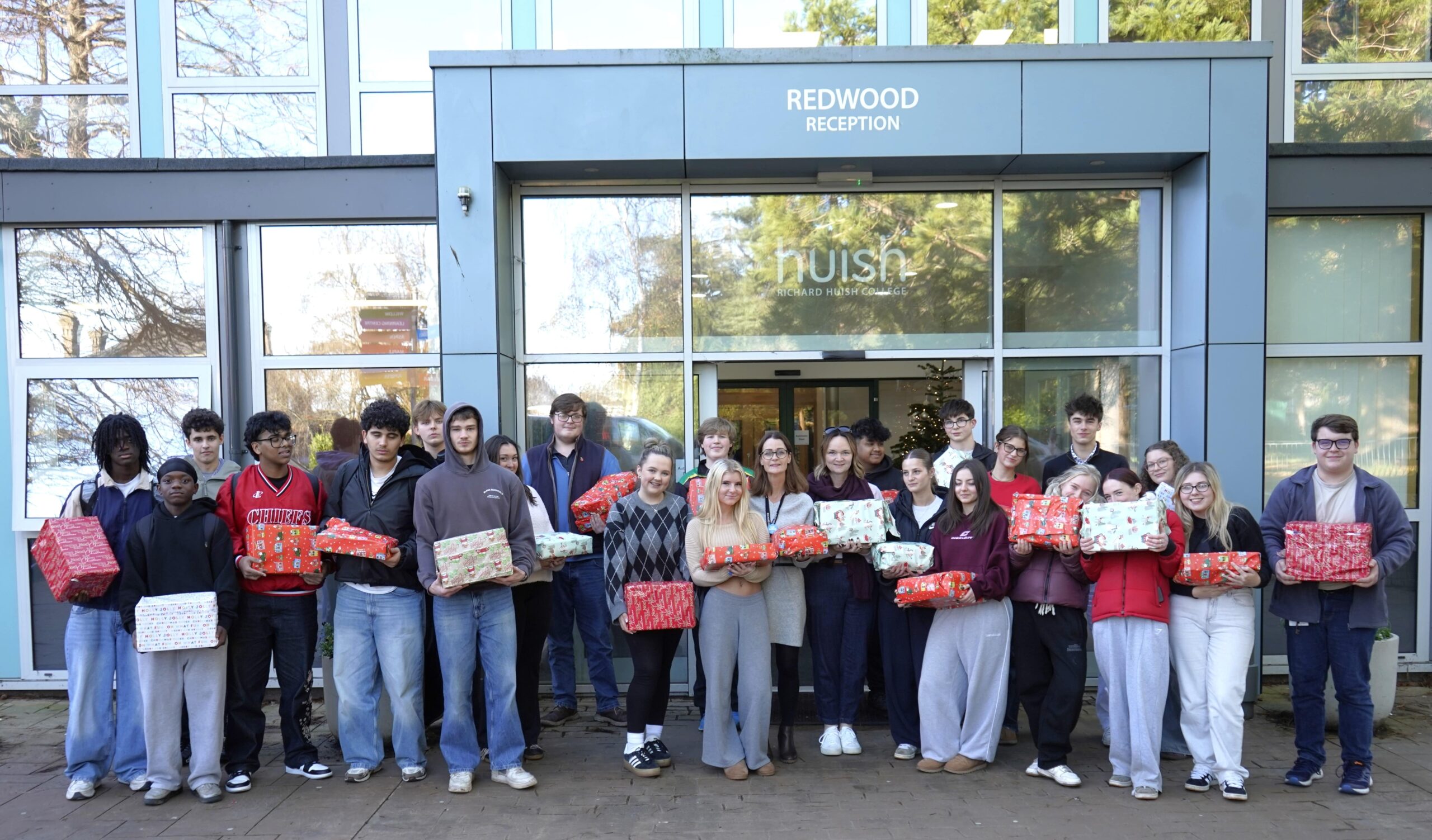 Students and staff standing outside of the front of Huish holding presents wrapped for the Help Thy Neighbour appeal.