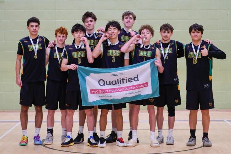 Group of athletes holding a 'Qualified AOC Sport National Championship' banner in a gymnasium, celebrating with thumbs up and smiles.