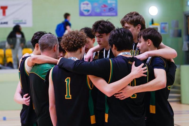 A basketball team in green and gold uniforms huddling together on the court.