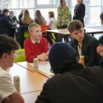 Students sit around a table with drinks and paper at a workshop.