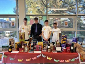 Four people stand behind a table filled with bingo prizes, including alcohol, chocolate and a cuddly toy. The front of the table is decorated with colourful bunting.