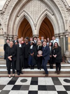 The Huish Law School mooting team and supporters pose inside the Royal Courts of Justice, standing beneath ornate stone arches, with students wearing court dress and holding the national trophy