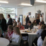 Prizegiving room set-up, with people sat chatting at tables. There are balloons on tables