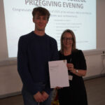 A prize-winning student stands with Emma Fielding, they are holding the student's certificate and smiling.