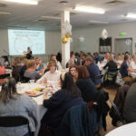 Prizegiving room set-up, with people sat chatting at tables. There are balloons on tables
