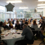 Prizegiving room set-up, with people sat chatting at tables. There are balloons on tables