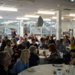 Prizegiving room set-up, with people sat chatting at tables. There are balloons on tables