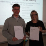 A prize-winning student stands with Emma Fielding, they are holding the student's certificates and smiling.
