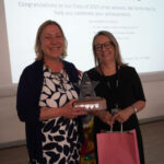 A sponsor representative holds a trophy and stands next to Emma Fielding, who is holding a pink gift bag.
