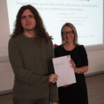 A prize-winning student stands with Emma Fielding, they are holding the student's certificate and smiling.