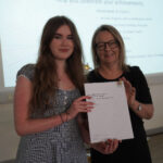 A prize-winning student stands with Emma Fielding, they are holding the student's certificate and smiling.