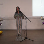 Dr Amber Leach gives a speech. She is stood at a lectern between two large balloon towers.