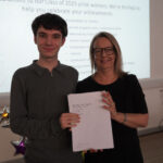 A prize-winning student stands with Emma Fielding, they are holding the student's certificates and smiling.