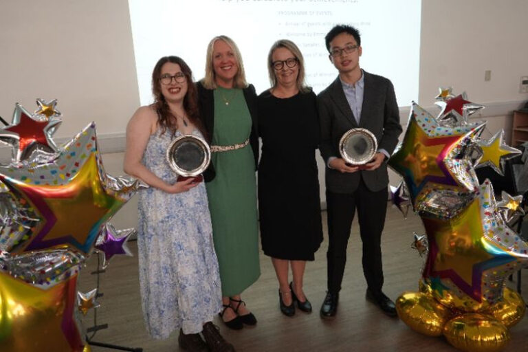 Students and staff pose for a photo with their awards. Balloon stands are either side.