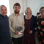 A prize-winning student stands with a parent, sponsor and teacher. They are smiling. The student holds his trophy.