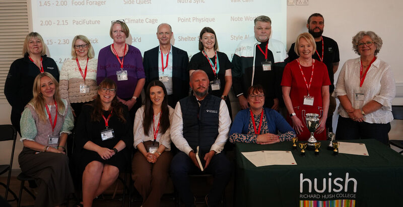 A large group photo of the 'dragons' seated and standing behind an awards table.
