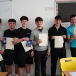 A group of students stand holding certificates and bags of chocolate in a classroom.