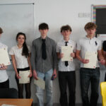 A group of students stand holding certificates in a classroom.