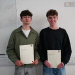 2 students stand holding certificates in a classroom.