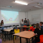 A student team presents in front of a classroom screen reading “Side Quest.”