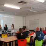 Four students present a slide titled “Distribution Channels” to seated judges.