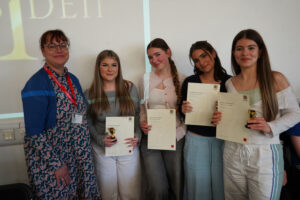 Four students stand holding certificates and small trophies beside Bethan Turner.