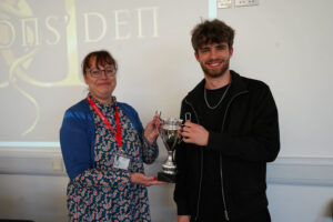 Two people standing indoors holding a large silver trophy during an awards presentation.