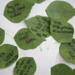 Collection of green paper leaves featuring handwritten pledges related to environmental actions, such as reducing plastic use and picking up litter.